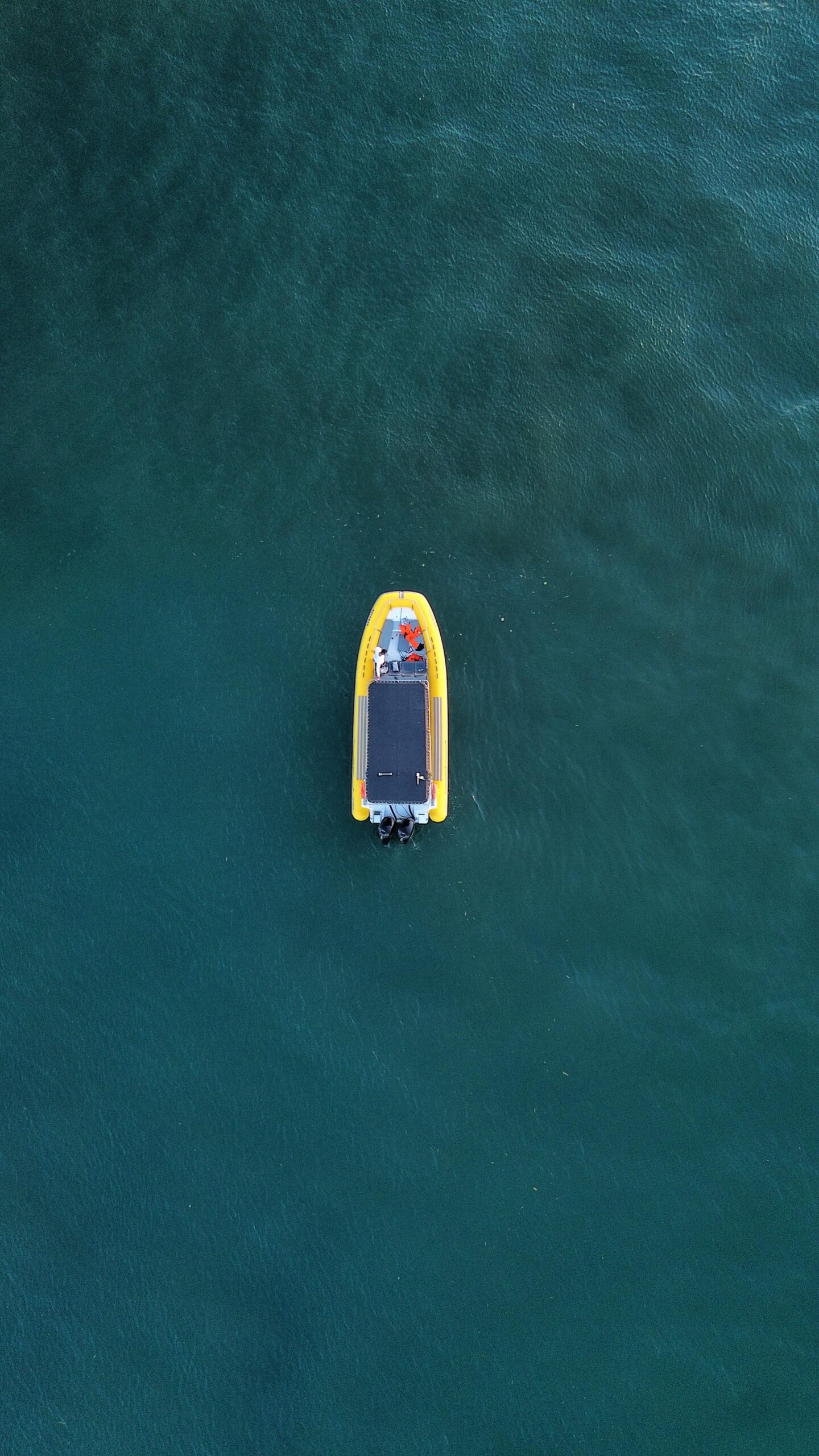 Barco inflável amarelo visto de cima flutuando em águas profundas azul-esverdeadas, sem outras embarcações ao redor.